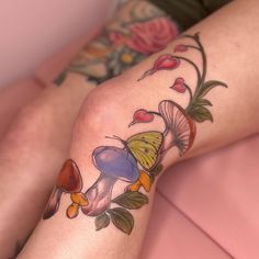 a woman's legs with tattoos on them and flowers around her ankles, sitting on a bed