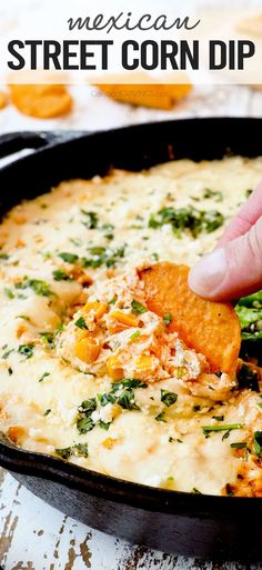 a hand dipping a tortilla chip into a bowl of mexican street corn dip