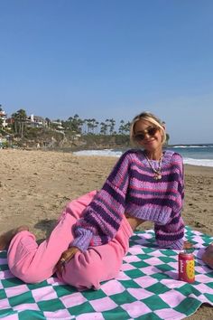 a woman sitting on top of a green and white checkered blanket next to the ocean