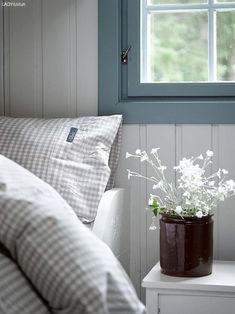 a vase with flowers sitting on top of a white table next to a pillow and window