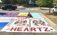 a man sitting on top of a giant playing card game in the middle of a parking lot