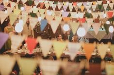 many people are sitting at tables with colorful flags hanging from the ceiling and plates on the table