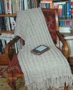 a blanket sitting on top of a wooden chair in front of a bookshelf