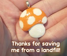 a hand holding a small orange and white mushroom pendant with words thanks for saving me from a landfill