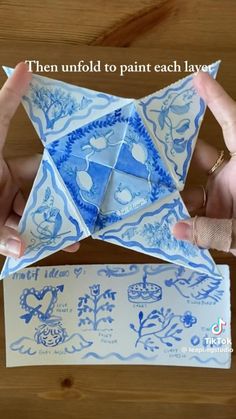 two hands holding an origami piece with blue and white designs on the bottom