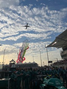 a group of people standing in front of an air plane flying over the sky with colorful kites