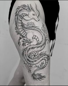 a black and white photo of a dragon tattoo on the thigh, with flowers around it