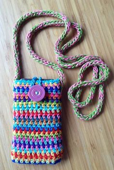 a crocheted purse with a pink button on the front and green, blue, red, yellow, and purple straps