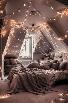 an attic bedroom with string lights strung from the ceiling and blankets on the bed in front of the window