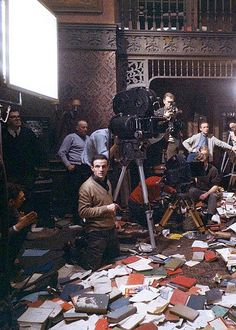 a group of people sitting around a pile of books and papers in a room full of other people