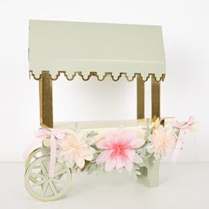 a small cart with flowers on the front and wheels, painted pink and white in shades of pale green