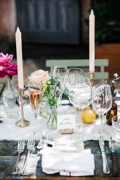 the table is set with wine glasses, silverware and flowers in glass vases