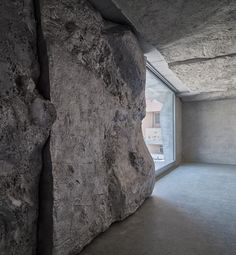 an empty room with large rocks on the wall and windows to the outside, in front of a window that looks out onto a street