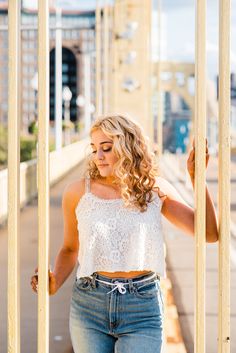 a woman in jeans and a white top is leaning against a fence with her hands on the bars