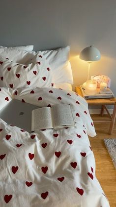 an open laptop computer sitting on top of a white bed covered in red heart print sheets