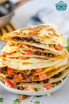 a stack of quesadillas sitting on top of a white plate covered in meat and cheese