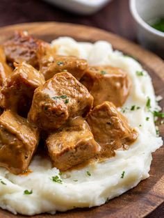 a wooden plate topped with mashed potatoes and meat