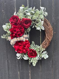 a wreath with red flowers and greenery hanging on a wooden wall next to a fence