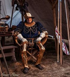 a man dressed in armor sitting on top of a chair next to a wooden pole