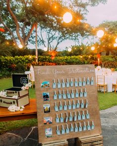 a wooden sign sitting on top of a lush green field next to a table covered in bottles