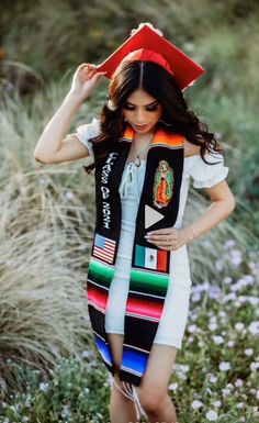 a woman wearing a graduation cap and gown standing in the grass with her hands on her head