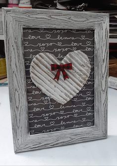 a white heart with a red bow on it sitting in a frame next to other items