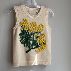 a white sweater with yellow flowers on it hanging from a clothes hanger next to a wall