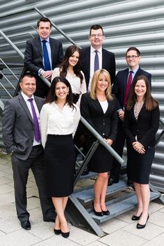 a group of business people standing in front of a metal structure with stairs and railings