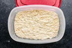 a red container filled with dough sitting on top of a black counter next to a red lid