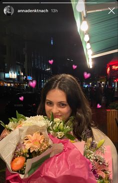 a woman holding flowers in her hands and looking at the camera with hearts flying around