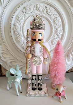 a nutcracker, deer and toy figurine sitting on a table in front of a white wall