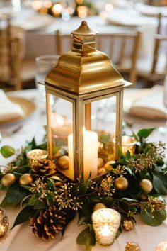 a lantern is sitting on top of a table with greenery and pineconis