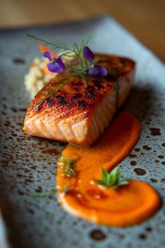 a piece of salmon on a plate with sauce and garnishes around it