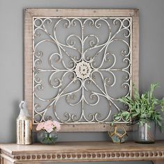 an ornate metal wall decoration with flowers and vases on a table in front of a gray wall