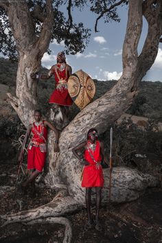 two men dressed in red standing next to each other near a large tree with an animal on it