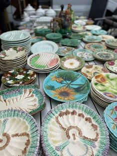 many plates are sitting on a table with flowers and leaves painted on them, all in different colors