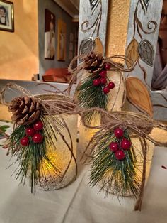 three mason jars decorated with pine cones and red berries are sitting on a white table cloth