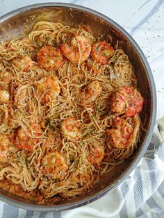 a pan filled with pasta and shrimp on top of a white table cloth next to a fork