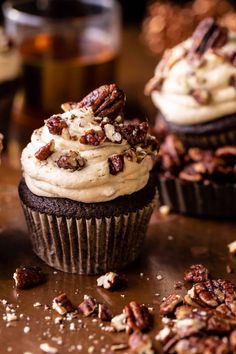 two cupcakes with frosting and pecans scattered around them on a table