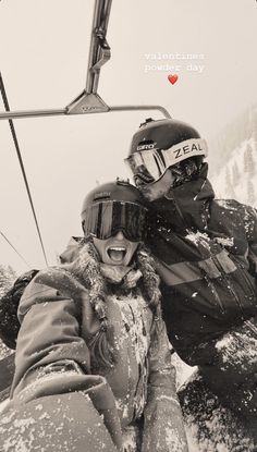 a man and woman sitting on top of a ski lift in the snow with their arms around each other