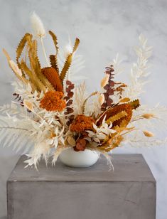 an arrangement of dried flowers in a white vase on a gray table top with grey background