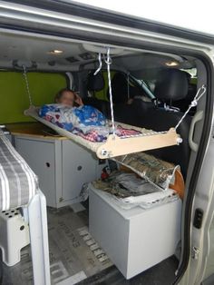 a man sleeping in the back of a van next to an open trunk and bed