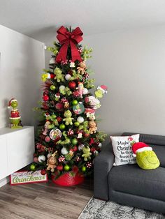 a decorated christmas tree in a living room next to a gray couch and white wall