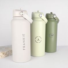 three different colored water bottles sitting next to each other on a white counter top,