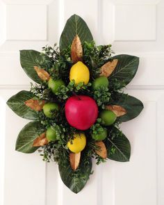 a wreath with fruit and leaves hanging on the front door to decorate it's entrance