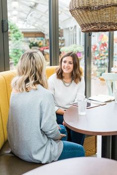 two women sitting at a table in a restaurant talking to each other and smiling for the camera