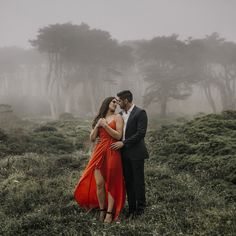 a man and woman standing in the middle of a field on a foggy day