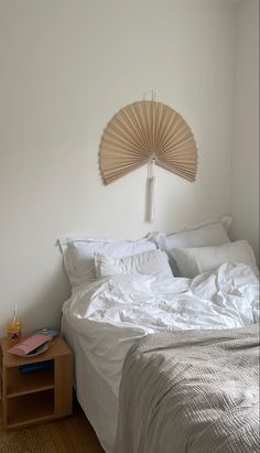 a bed with white linens and a wooden fan on the headboard above it