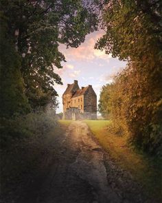 an old house sitting on the side of a dirt road in front of some trees