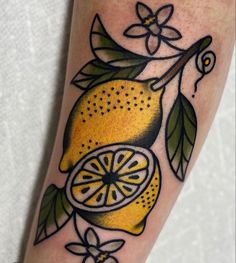 a lemon tattoo on the leg with leaves and flowers around it's edges is shown